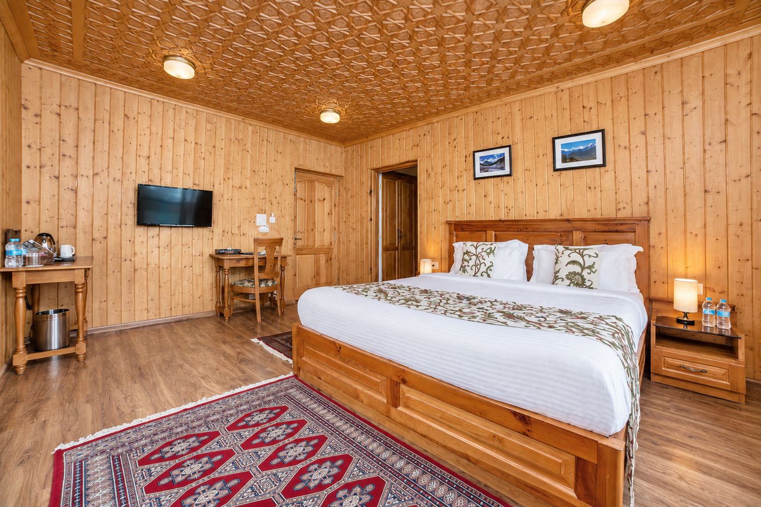 Una habitación con paneles de madera, una cama, un escritorio, un televisor y una puerta.