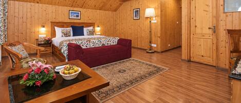 Una habitación de madera con una cama, un sofá rojo, una mesa con flores y una alfombra estampada.