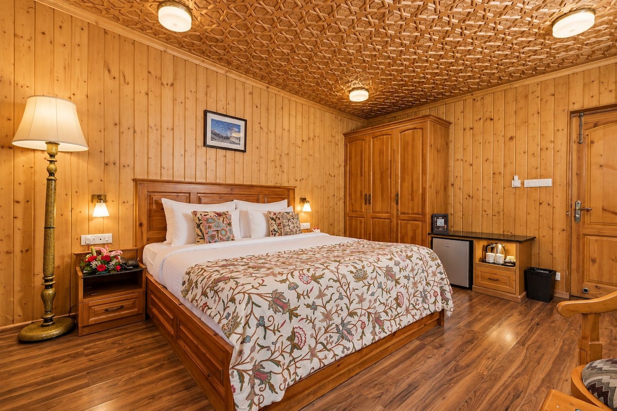 Quarto com painéis de madeira, cama, abajures, mesa de cabeceira, cômoda e uma pequena cozinha.