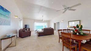 A spacious living area with a large window, a ceiling fan, a dining table with chairs, and a television.