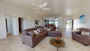 A spacious living room with a sectional sofa, a glass coffee table, and a ceiling fan.