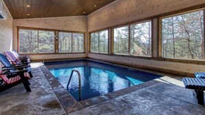 A wooden cabin with a swimming pool, large windows, and lounge chairs.