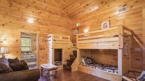 A cozy cabin interior with wooden walls, a sofa, a table, and bunk beds.