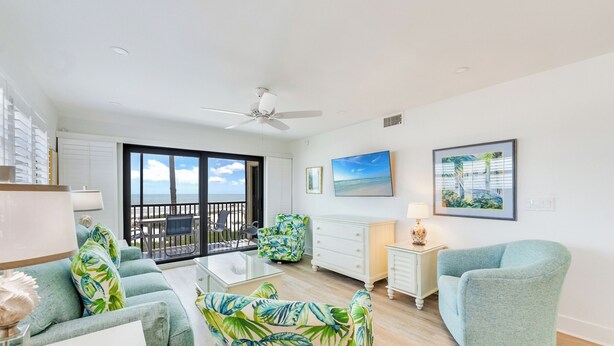 A spacious living room with a balcony, a ceiling fan, and a view of the ocean. - OCEAN'S REACH 1D2: 2-Bedroom, Corner Unit, Dunes Golf Privileges! (Sanibel Island)