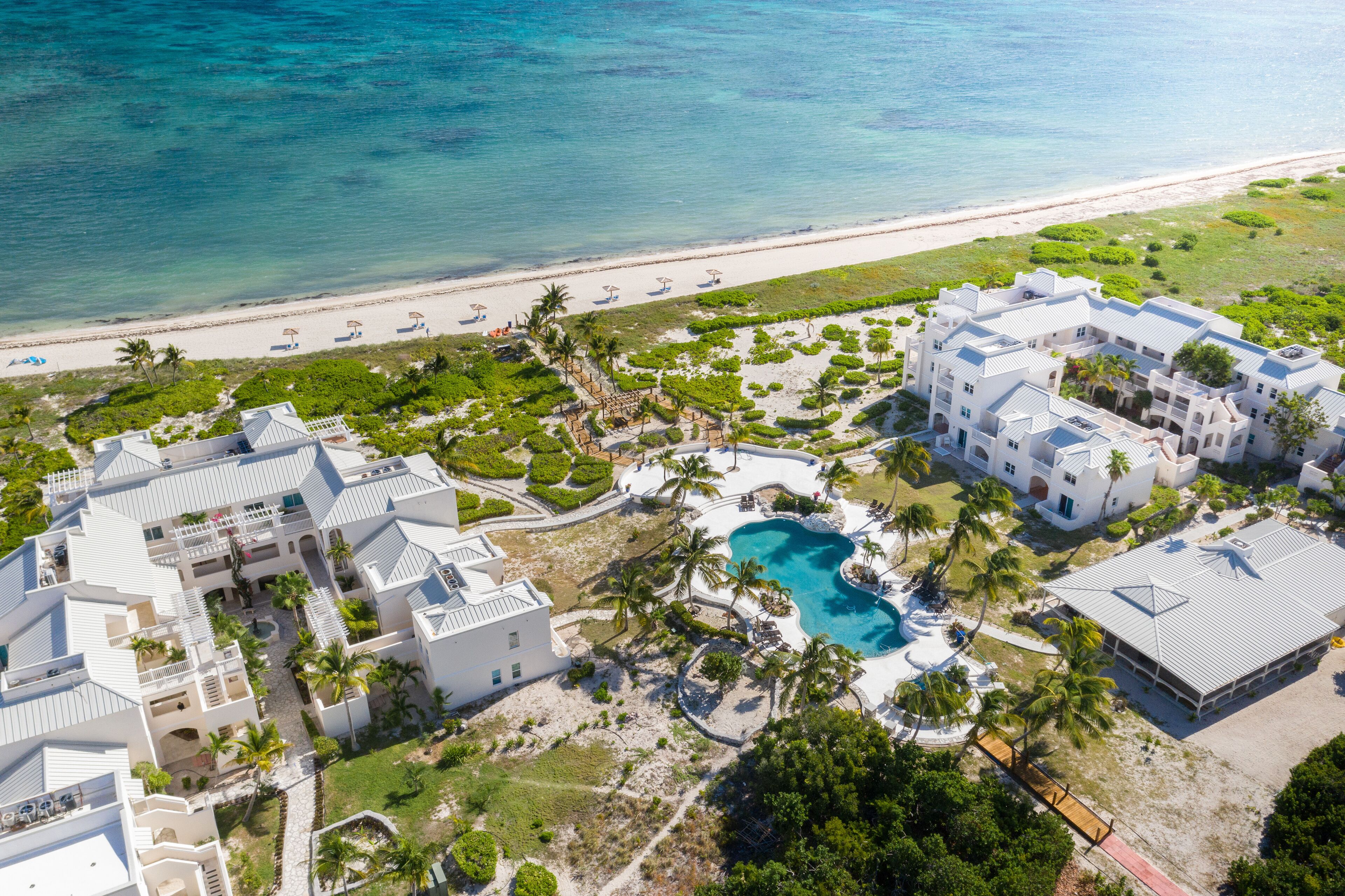 An aerial view of a resort with multiple buildings, a swimming pool, and a beach.