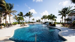 A swimming pool with a curved edge, surrounded by palm trees and lounge chairs.