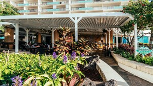 Een hotel lobby met een overdekt terras, diverse planten en een bord met de tekst 'Cinnamon's'.