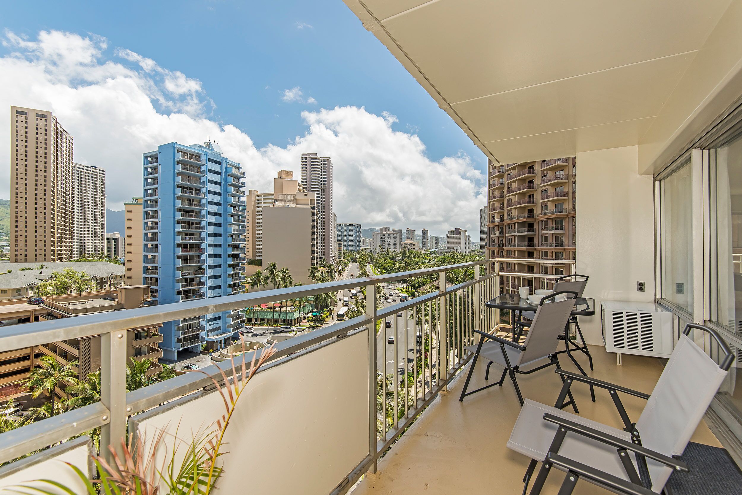 A balcony with a table and chairs, overlooking a cityscape with high-rise buildings and a clear sky.
