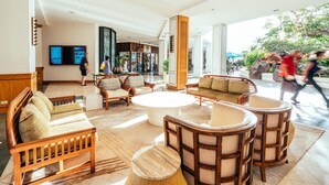 Een ruime lobby met een centrale salontafel, een zithoek met banken en stoelen, en een groot televisiescherm.