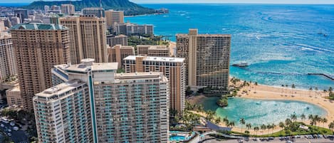 A high-rise hotel with multiple floors, a beach, and a clear view of the ocean.