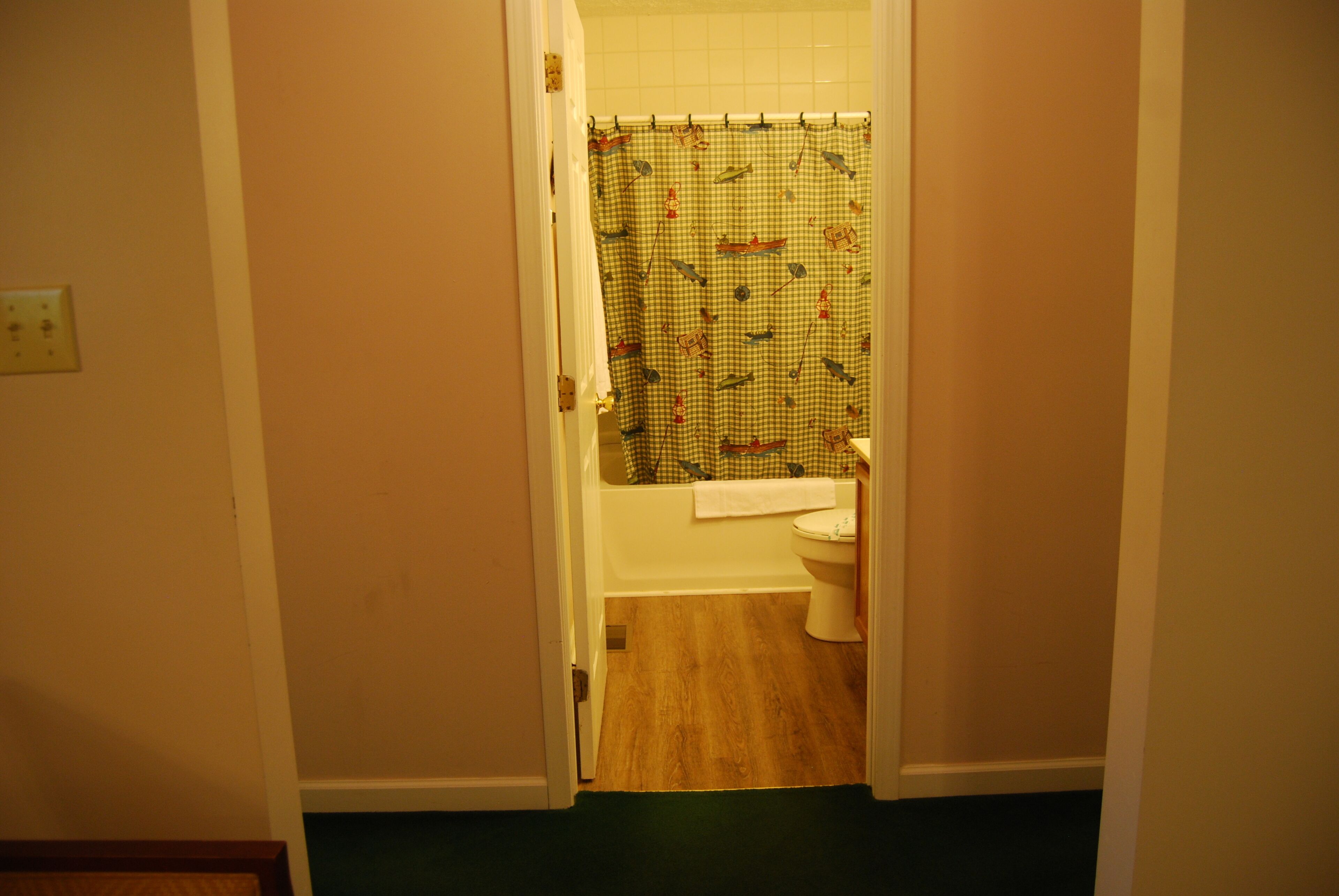 A bathroom with a checkered shower curtain, a white toilet, and a wooden floor.