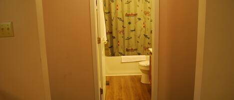 A bathroom with a checkered shower curtain, a white toilet, and a wooden floor.