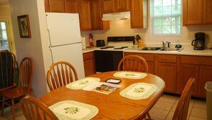 A kitchen with wooden cabinets, a white refrigerator, a stove, and a sink. There are four wooden chairs around a table with placemats.