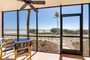 A room with large windows overlooking a beach, featuring a ceiling fan, wicker chairs, and a table. - OCEAN'S REACH 4B1: Ground-Level, Easy/Direct Beach Access, All Amenities Open (Sanibel Island)