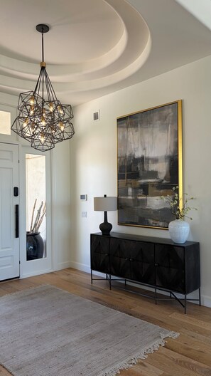 A modern interior with a geometric chandelier, a large abstract painting, a console table with a vase, and a textured rug.