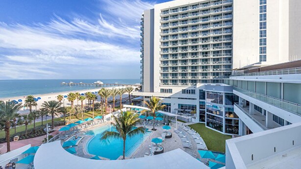 A hotel with a pool, palm trees, and a view of the ocean.