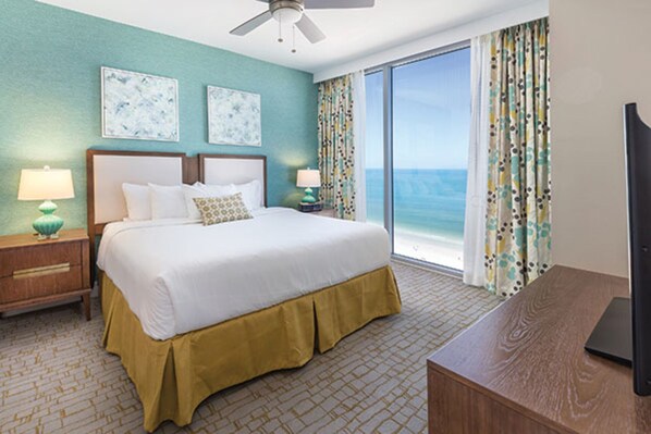 A hotel room with a large bed, two nightstands, a desk, and a view of the ocean.