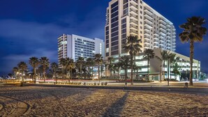 A beachfront hotel with multiple floors, palm trees, and a sandy beach.