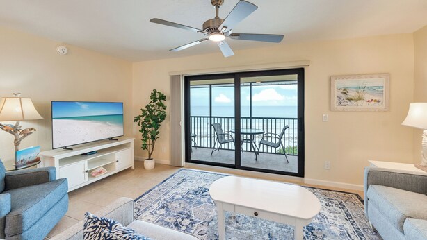 A living room with a TV, sofa, coffee table, and a balcony with a view of the ocean. - OCEAN'S REACH 2B4: 1-Bdrm, Top Floor w/Gorgeous Views, All Amenities Open! (Sanibel Island)
