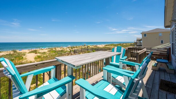 A wooden deck with turquoise chairs and a table overlooking a beach with sand dunes and the ocean. - Beachfront Home- Amazing Oceanfront w/ Hot tub!!! Sleeps 8- Free Wifi! -6 beds (Kill Devil Hills)