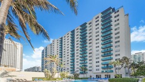 A high-rise hotel with multiple balconies, a swimming pool, and palm trees.