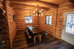 A log cabin interior with a wooden dining table, benches, and a ceiling light fixture. - Full Log Home On Private Lake Close To Town, Snowmobile Trails, & Golf Course (Mercer)