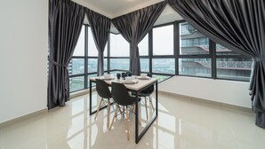 A modern dining area with a table set for four, large windows with curtains, and a city view. - OYO Home 44045 Splendid 2br Arte Plus (Kuala Lumpur)