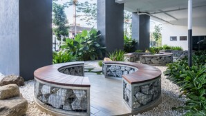 A modern outdoor seating area with circular wooden tables and stone walls, surrounded by pebbles and greenery. - OYO Home 44045 Splendid 2br Arte Plus (Kuala Lumpur)
