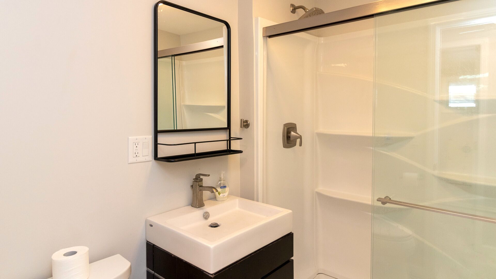 Un bany amb un rentatge blanc, un mirall i una cabina de dutxa de vidre.