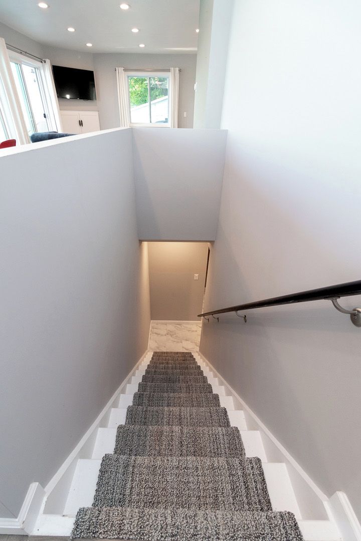 Una escalera con rellano alfombrado y barandilla, que conduce a una habitación con televisor y armarios.