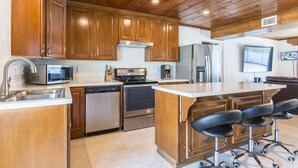Una cocina con gabinetes de madera, electrodomésticos de acero inoxidable, lavavajillas y una zona de bar con taburetes.