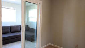 A room with a sliding glass door leading to a balcony, a grey sofa, and a carpeted floor.