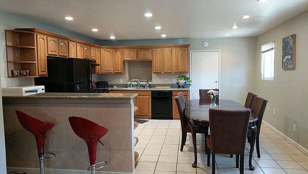 A modern kitchen with wooden cabinets, a black refrigerator, a dishwasher, and a dining area with a table and chairs.