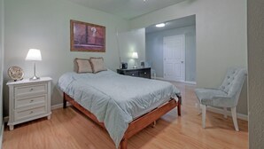 A bedroom with a bed, nightstands, a chair, a dresser, a ceiling fan, and a door leading to another room.