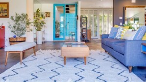 Een moderne woonkamer met een blauwe bank, een houten salontafel en een witte vloerkleed met blauwe patronen.