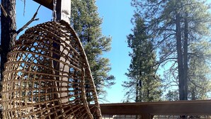 A wicker hanging chair with a cushion, a wooden railing, and a view of trees and a parking lot. - Stunning New Contemporary Home Minutes to Downtown Flagstaff (Flagstaff)