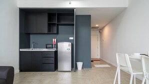 A modern kitchen with dark cabinets, a microwave, and a refrigerator. There is a white dining table with chairs and a small white trash bin. - OYO Home 43951 Fair  Studio Empire City Marriot (Petaling Jaya)