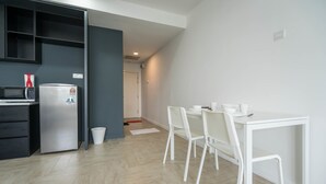 A modern kitchen with a refrigerator, microwave, and cabinets. There is a dining area with a white table and chairs. - OYO Home 43951 Fair  Studio Empire City Marriot (Petaling Jaya)