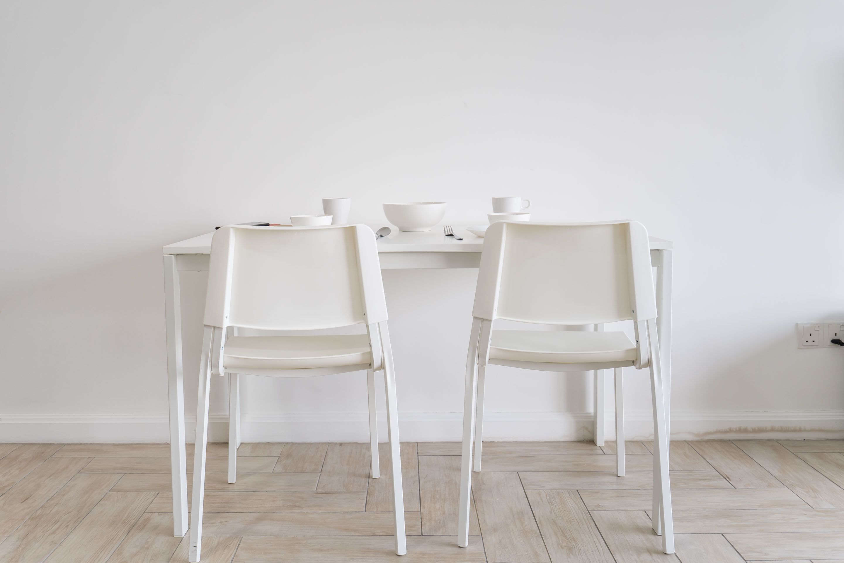 A minimalist dining area with two white chairs and a table, featuring a white bowl and cups.