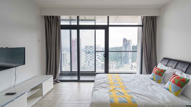 A modern hotel room with a large bed, a TV on a stand, and a view of the city through large windows. - OYO Home 43951 Fair  Studio Empire City Marriot (Petaling Jaya)