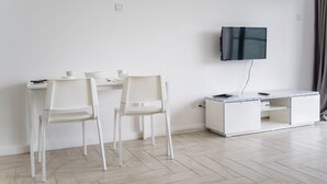 A minimalist living room with two white chairs, a white desk, a flat-screen TV mounted on the wall, and a white cabinet with drawers. - OYO Home 43951 Fair  Studio Empire City Marriot (Petaling Jaya)