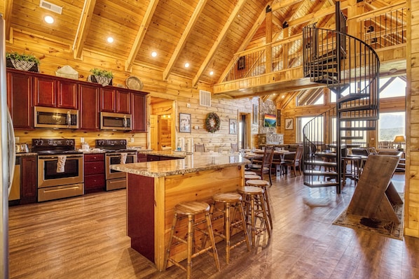 A spacious kitchen with a central island, wooden bar stools, and a spiral staircase.