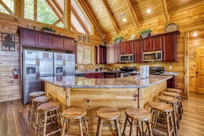 A wooden cabin interior with a kitchen featuring a large island, bar stools, and a fire extinguisher.