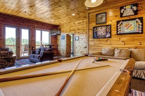 Interior de madera con mesa de billar, sofá y juegos de mesa enmarcados.