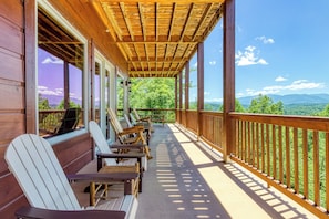 A wooden deck with Adirondack chairs, a wooden railing, and a view of mountains.