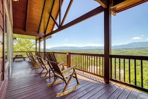 A wooden deck with rocking chairs and a view of mountains.