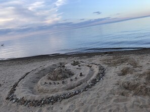 A sandy beach with a circular stone arrangement. - Sunrise in Sandy Beach Property 1 (Harbor Beach)