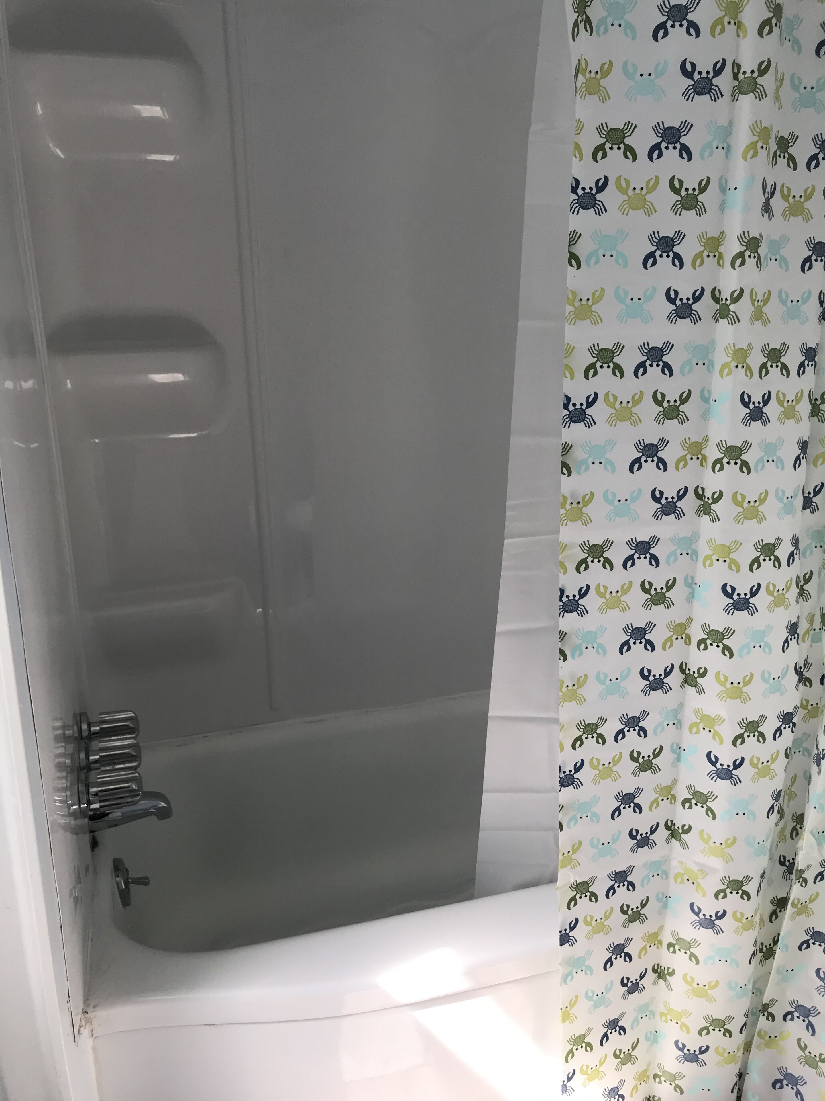 Un baño con bañera, cortina de ducha con motivos de cangrejo y mampara de vidrio.