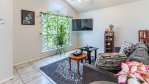 Ein Wohnzimmer mit Deckenventilator, einem an der Wand montierten Fernseher, einer Topfpflanze, einer Couch und einem Couchtisch.