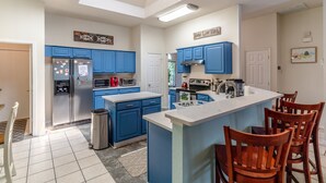 Eine moderne Küche mit blauen Schränken, einem Edelstahl-Kühlschrank, einem eingebauten Ofen und einer großen Kochinsel mit Barhocker.